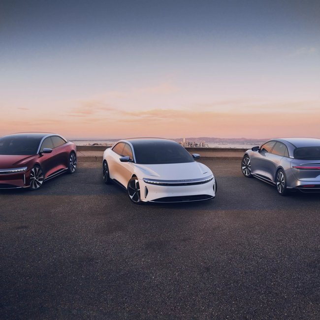 Three Lucid Air at sunset on concrete with a desert behind them in the distance.